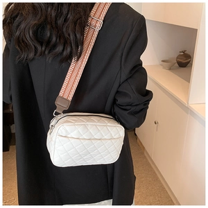 Detail of white quilted crossbody bag with brown geometric pattern wide strap worn by a model