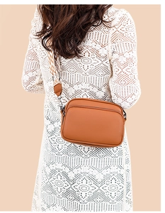 Brown lychee grain crossbody bag with a wide geometric pattern woven strap on white dress
