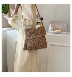 Detail of hand-woven straw crossbody bag with delicate shell pattern and side tassel fringe