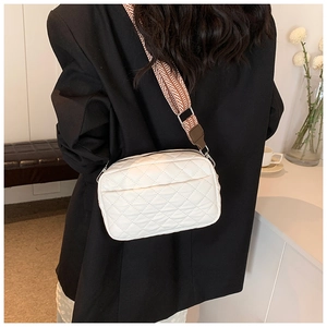 Close-up of white quilted crossbody bag with stylish woven strap on black blazer outfit