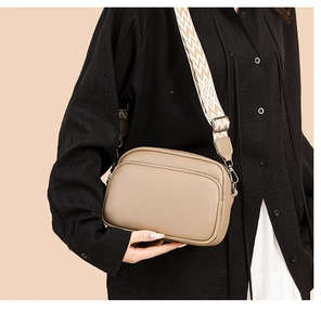 Detail view of khaki pebbled leather crossbody bag with dual zippers and wide patterned strap