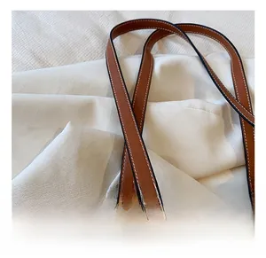 Détail de la texture paille tressée avec poignée en cuir marron et surpiqûres blanches du sac