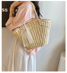 Detail of woven straw tote bag featuring decorative floral lace ribbons on the side