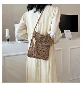 Detailed close-up of brown straw woven crossbody bag with hollow weave and side tassel