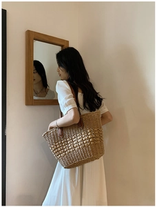 Détail du sac cabas en paille tissée main avec anses en cuir marron dans un décor d'été