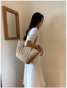 Détail d'un sac cabas en paille tissée avec bandoulières en cuir marron et motifs texturés