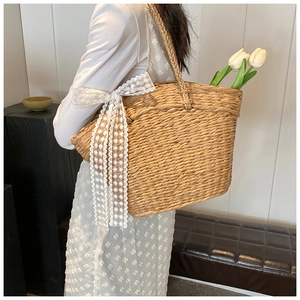 Detail of hand-woven straw tote bag featuring a large white lace bow and floral embroidery