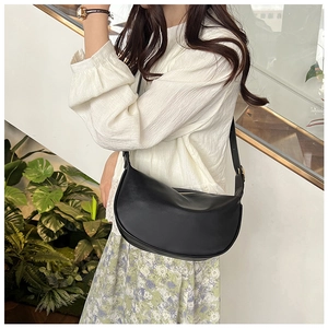 Chic black half-moon PU leather crossbody bag worn by a model in a natural outdoor setting