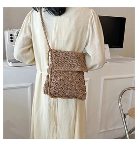 Detailed close-up of straw woven crossbody bag with tiered patterns and long tassels