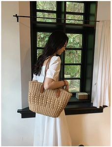 Détail d'un sac cabas en paille tissée avec poignées en cuir marron sur l'épaule du modèle
