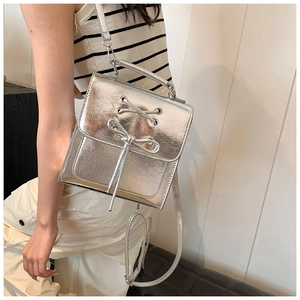 Close-up of a metallic silver PU leather backpack with bow detail worn by a model