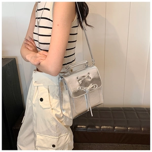 Detail view of a metallic silver mini bag with cross-lace design and bow accent decoration