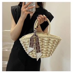 Detail of handmade straw tote bag featuring decorative patterned silk scarf and woven handles