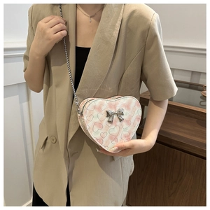 Détail d'un sac bandoulière rose en forme de cœur avec nœud argenté et chaîne en métal