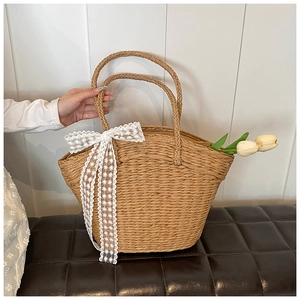Detail of woven straw handbag featuring white lace bow and decorative tulips inside