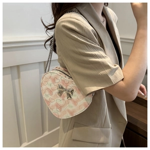 Détail du sac en forme de cœur rose avec motif marbre et nœud argenté sur blazer beige