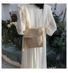 Detail of a woven straw crossbody bag with fringe tassels on a model in nature