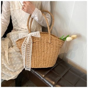 Detail of hand-woven straw tote bag featuring white lace ribbon and floral accents