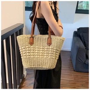 Détail d'un sac cabas en paille tressée beige avec anses en cuir marron et textures