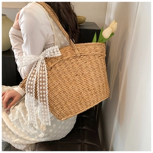 Close-up of woven straw shoulder bag featuring elegant white lace bow and floral accents