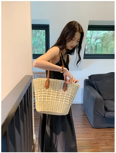 Détail d'un grand sac cabas en paille avec anses en cuir marron porté par un mannequin