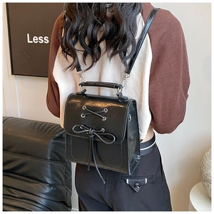 Detail of black PU leather backpack showing decorative cross-lacing and elegant bow accent