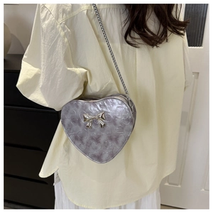 Détail du sac bandoulière argenté en forme de cœur avec motifs gaufrés et nœud miroir chic