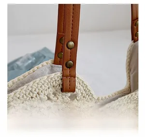 Detail of woven knit handbag showing bronze rivets and brown leather strap on cream body