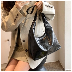 Dettaglio della borsa hobo nera lucida con goffratura su completo beige