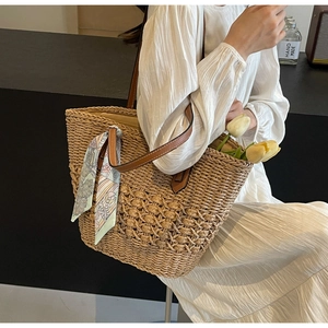 Detailed texture of straw tote bag featuring leather straps and decorative silk scarf detail