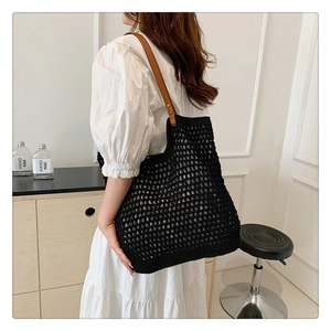Detailed close-up of a black knit crochet tote bag with brown leather straps for women