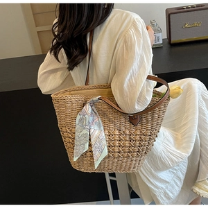 Detail of straw woven tote bag featuring blue silk scarf and brown leather handles