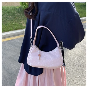 Detail of pink floral embossed crossbody bag with bead charm in natural outdoor setting