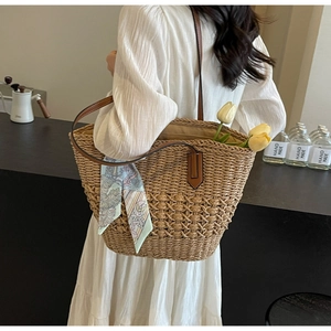 Detail of hand-woven straw tote bag with brown leather straps and floral scarf accent