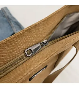 Detail shot of the silver metal zipper and khaki canvas fabric texture of the handbag