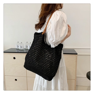 Detail view of black knit tote bag with brown leather straps worn by a model