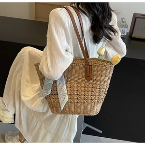 Detail of woven straw tote bag with brown leather handles and decorative floral silk scarf