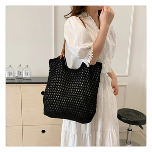 Detail of hand-woven black knit tote bag showing intricate crochet texture and brown leather strap