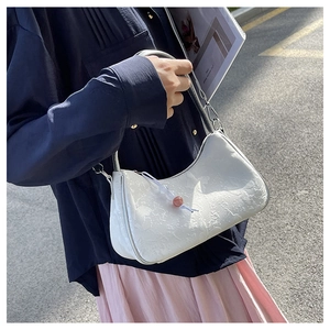 Close-up of white crossbody bag with floral texture, metal handle, and pink bead detail