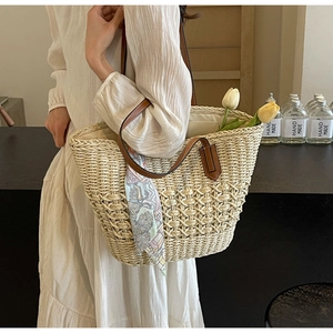Close-up of woven straw tote bag with brown leather handles and decorative silk scarf