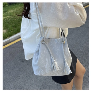 Détail d'un sac seau en cuir PU gris clair avec ornement à pompon et texture marbrée