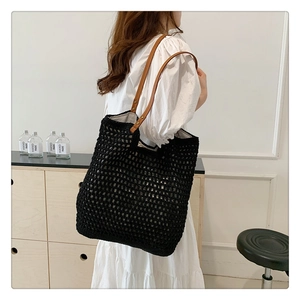 Detail of hand-knitted tote bag with brown leather handle shown in a minimalist home setting