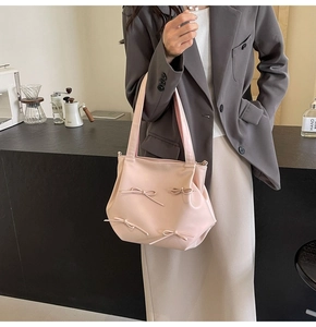 Pink PU leather crossbody bag with bow details styled by a model in a cafe setting
