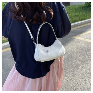 White embossed underarm bag with floral texture and pink bead zipper pull shown on model