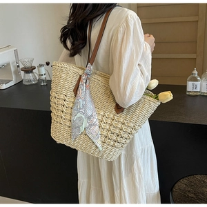Detail view of woven straw tote bag with brown leather straps and floral silk scarf