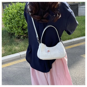 Detail of white jacquard hobo bag featuring a decorative orange bead and crossbody strap