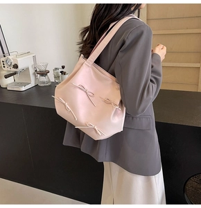 Detail of pink PU leather tote with 3D bow accents worn by a model in a minimalist room
