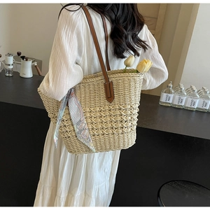 Detail of straw tote bag with brown leather handles and a decorative silk scarf