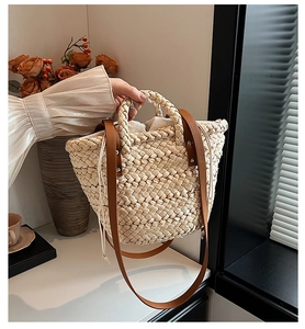 Detail of hand-woven straw tote bag featuring brown leather handles and drawstring lining
