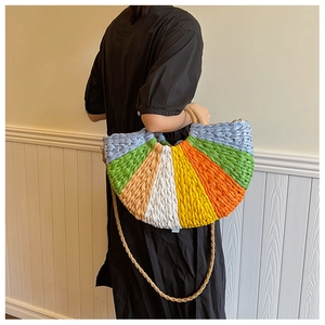 Rainbow woven straw bag displayed on model with colorful stripes and thin shoulder strap
